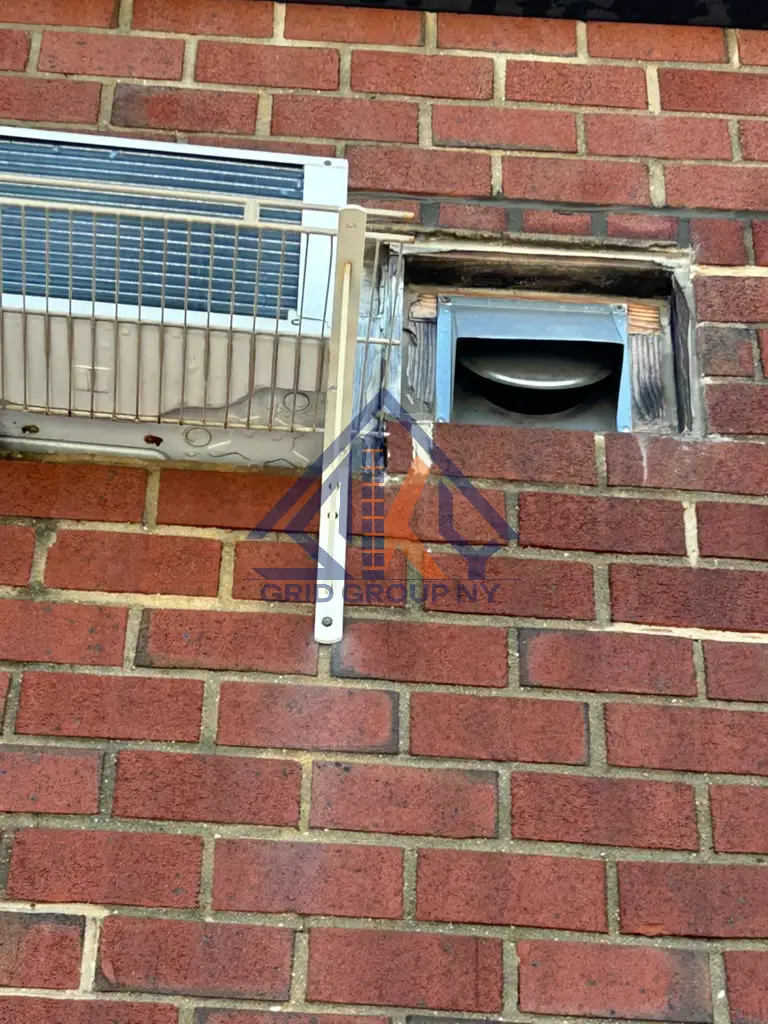 Vent opening beside an air conditioner sleeve with open joints around its frame on the Elmhurst brick facade